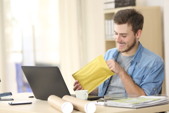 Young man smiling over a few shipping containers, arrayed around his laptop.