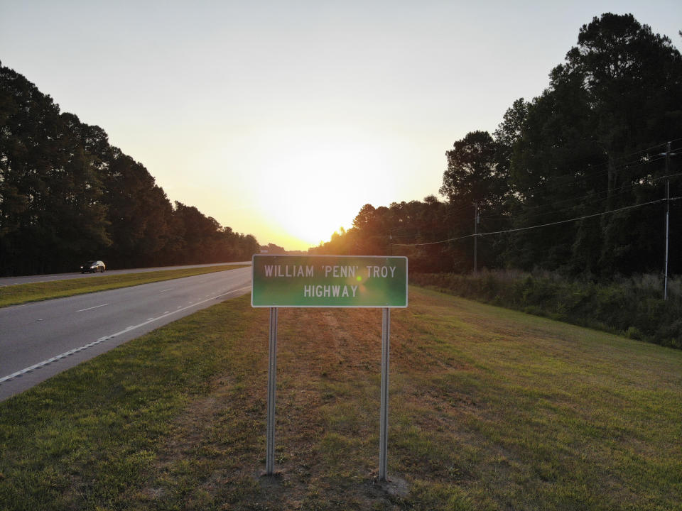 The sun rises behind a sign dedicating part of U.S. 76 in Mullins, S.C., to the late William Penn Troy Sr. on Monday, May 24, 2021. Over the years, Troy had served as a county commissioner, local school board member and church treasurer. But those were just his official duties. (AP Photo/Allen G. Breed)