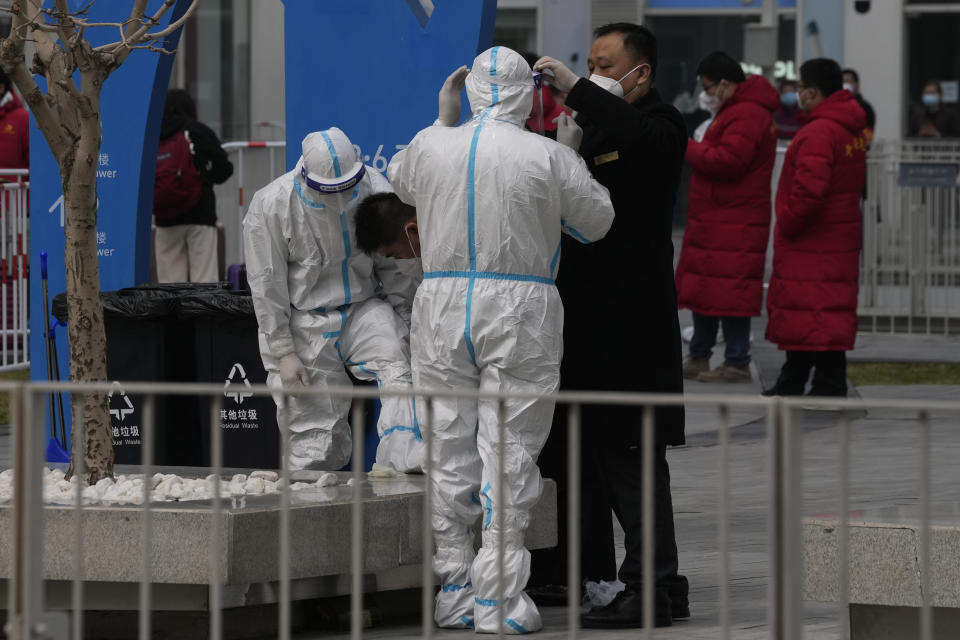 A security guard helps a worker put on protective gear outside an office building that was closed off after a case of coronavirus was detected on Sunday, March 13, 2022, in Beijing. The number of new coronavirus cases in an outbreak in China's northeast tripled Sunday and authorities tightened control on access to Shanghai in the east, suspending bus service to the city of 24 million and requiring a virus test for anyone who wants to enter. (AP Photo/Ng Han Guan)