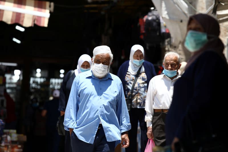 People wearing face masks to help fight the spread of the coronavirus disease (COVID-19) walk past shops in a market in Jerusalem's Old City