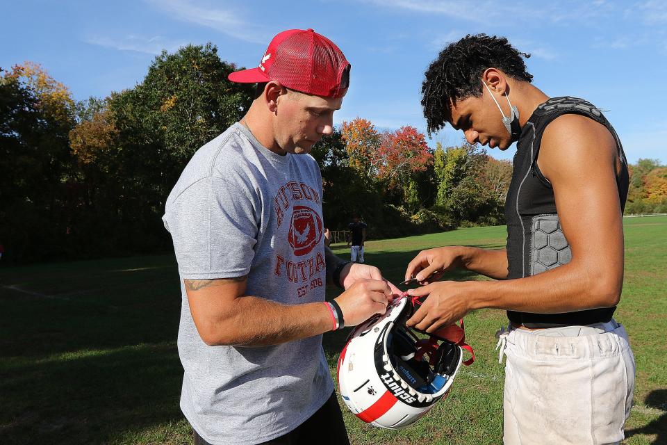 Hudson High assistant football coach Zac Attaway helps senior Marcus Bass, 17, fix his helmet before practice on Oct. 12, 2021.