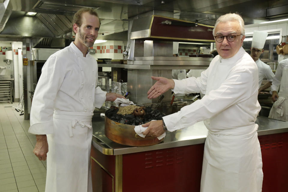 This Oct. 9, 2012 photo shows American Chef Dan Barber, left, and Alain Ducasse displaying a Cossabow Pig plate in the kitchen of the Plaza Athenee in Paris. He fires up the succulent pork over gnarled, carbonated pig bones, grows sweet greens in a soil mixed with pumice that's left over by the hazelnut oil industry and he's creating a new kind of wheat, named after himself _ Dan Barber. (AP Photo/Michel Euler)