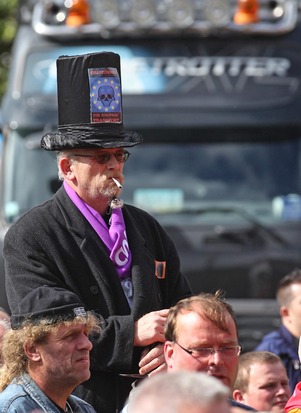 A trucker on stilts wears a high hat with a sticker that reads: 'Gravedigger for European Transport', during a protest in Brussels, Monday, Sept. 24, 2012. Truckers seek to disrupt morning traffic heading into the capital to protest competition from eastern Europe, which undercuts prices and lowers labor standards. (AP Photo/Yves Logghe)