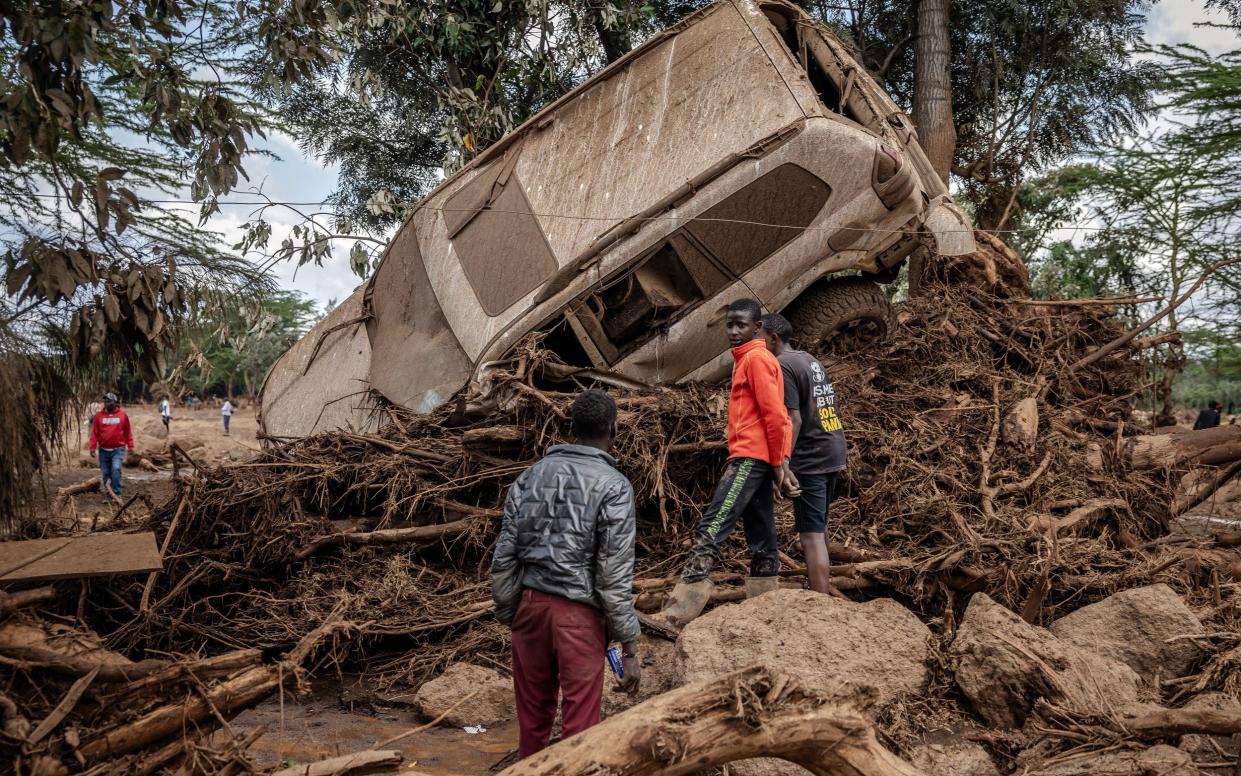Young men inspect a destroyed car carried by waters in an area heavily affected by torrential rains and flash floods in the village of Kamuchiri, near Mai Mahiu