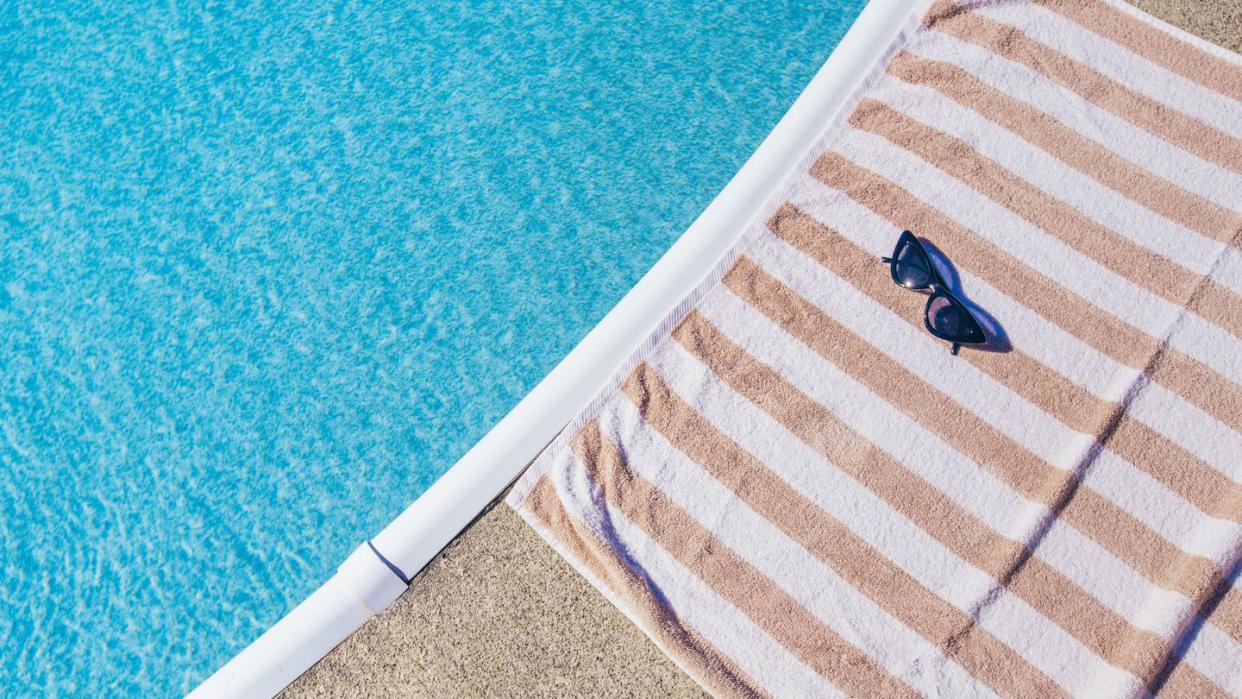 summer background striped beach towel with cateye sunglasses next to swimming pool