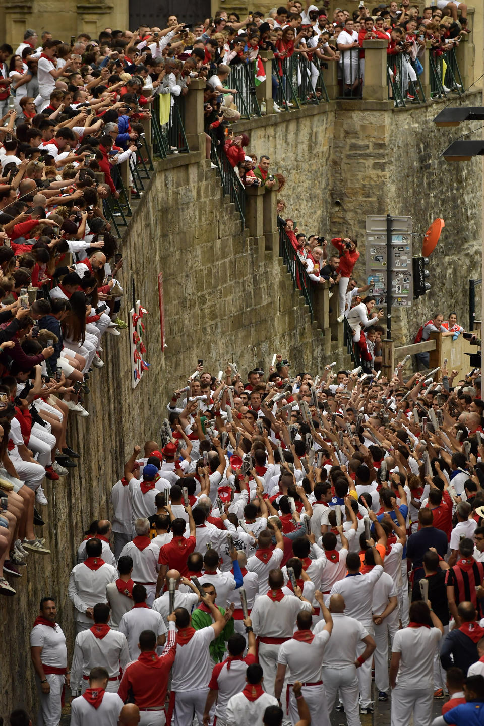 Revellers hold a rolled newspaper as they sing a song to San Fermin, bottom left, on Santo Domingo street ahead of the running of the bulls at the San Fermin Festival, in Pamplona, northern Spain, Sunday, July 7, 2019. Revellers from around the world flock to Pamplona every year to take part in the eight days of the running of the bulls. (AP Photo/Alvaro Barrientos)