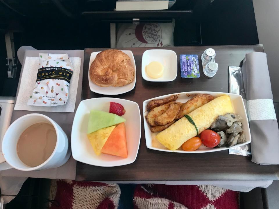 a breakfast on an airplane with egg, fruit, a roll, coffee on a tray
