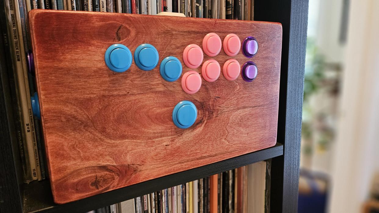  Custom wooden hitbox with bubblegum colored buttons on a bookshelf. 