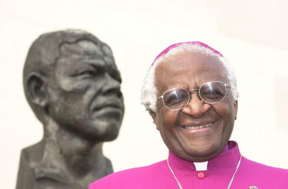 Archbishop Desmond Tutu stands next to a bust of former South African president Nelson Mandela in London in 2001 (William Conran/PA )