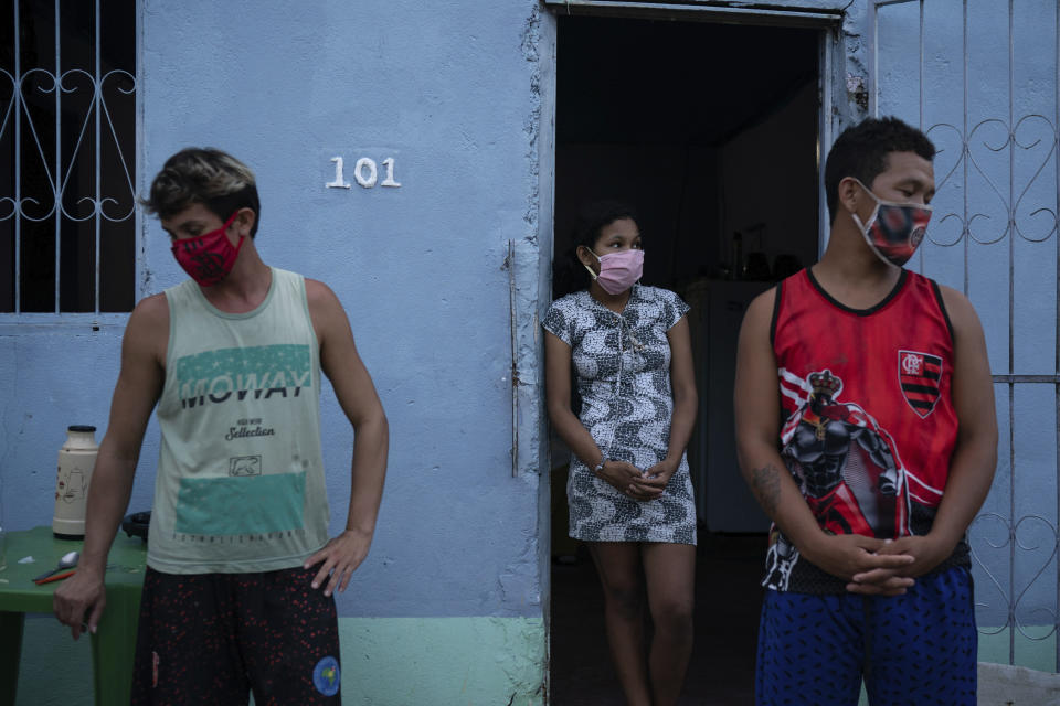 El cuidador Leandro Beiton (izquierda) y familiares del fallecido Edgar Silva, con mascarilla por la pandemia del coronavirus, parados ante la puerta de su casa luego de que operarios de SOS Funeral retiraron el cadáver de la vivienda, en Manaos, Brasil, el 12 de mayo de 2020. Según su familia, Silva padecía Alzheimer y murió en su casa tras dos días con fiebre y problemas para respirar. (AP Foto/Felipe Dana)