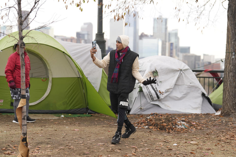 An occupant uses a mobile device during a city-sponsored sweep of an encampment overlooking the city skyline on Diamond Hill Wednesday, Nov. 1, 2023, in Denver. The sweep was just one of several staged in various locations across the Mile High City. (AP Photo/David Zalubowski)