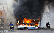 Dos motocicletas pasan junto a un autobús en llamas, incendiado por manifestantes de oposición que exigen saber el destino de los fondos de Petrocaribe, en Puerto Príncipe, Haití, el domingo 18 de noviembre de 2018. (AP Foto/Dieu Nalio Chery)