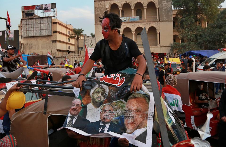 A masked protester hits a poster showing Iraqi politicians and militia leaders with a shoe, during ongoing anti-government protests in Baghdad, Iraq, Sunday, Nov. 3, 2019. (AP Photo)