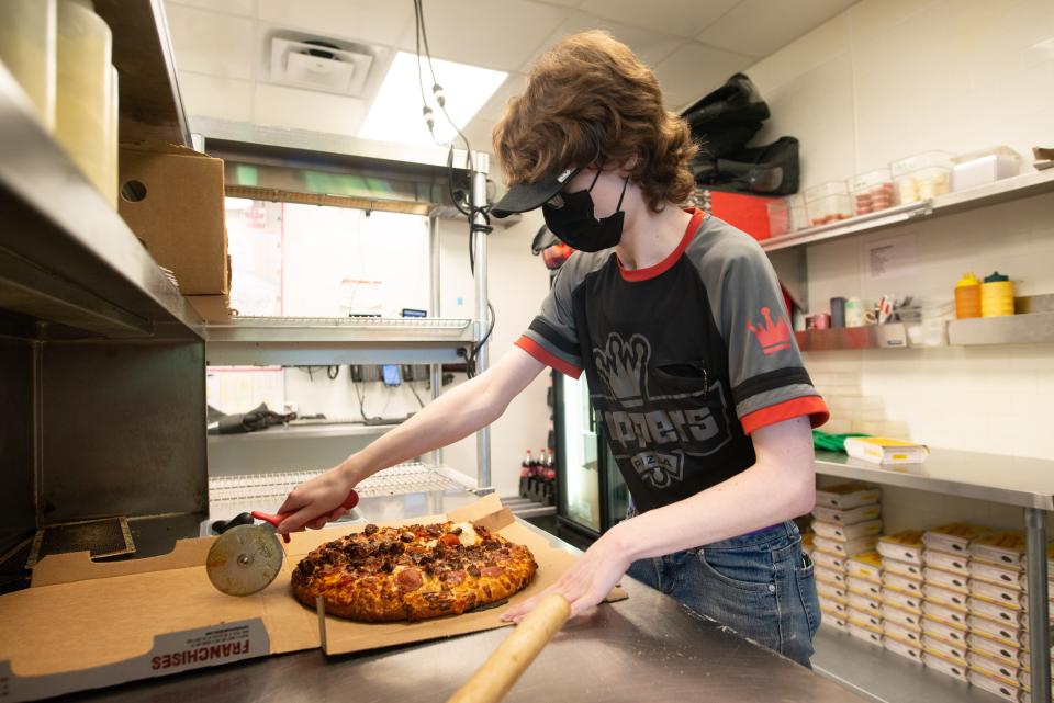 A Toppers Pizza employee in Lawrence cuts a pie for a delivery.