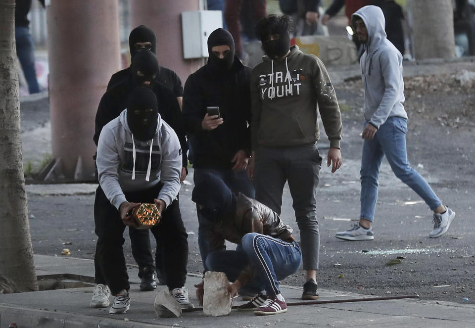 A supporter of the Shiite Hezbollah and Amal Movement groups, left, holds firecrackers to fire it against the riot policemen, as they trying to attack the anti-government protesters squares, in downtown Beirut, Lebanon, Saturday, Dec. 14, 2019. Lebanon has been facing its worst economic crisis in decades, amid nationwide protests that began on Oct. 17 against the ruling political class which demonstrators accuse of mismanagement and corruption. (AP Photo/Hussein Malla)