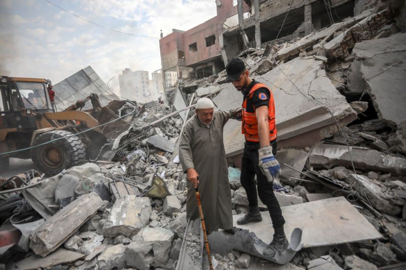 A Palestinian rescue workers helps a man walk amid destruction following Israeli airstrikes on a market in residential neighborhood in Khan Younis in the southern Gaza Strip on Tuesday. Photo by Ismael Mohamad/UPI