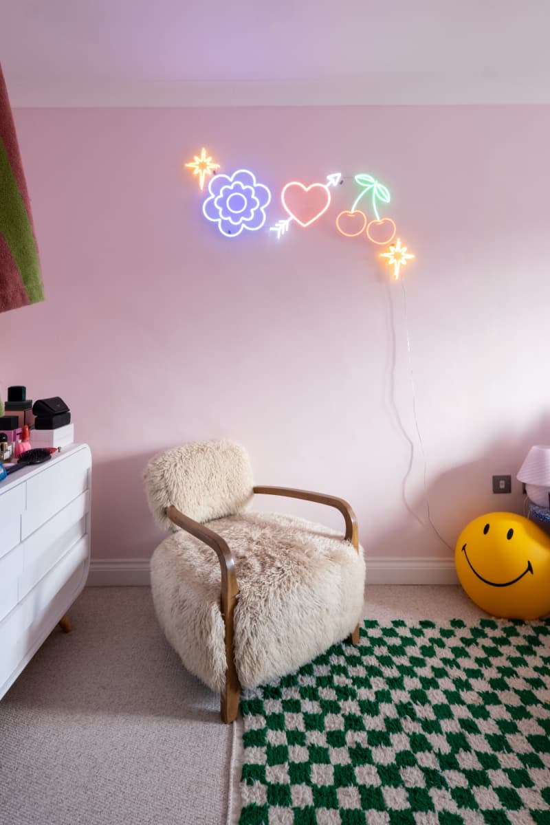 Neon lights hang above furry chair in pink bedroom.