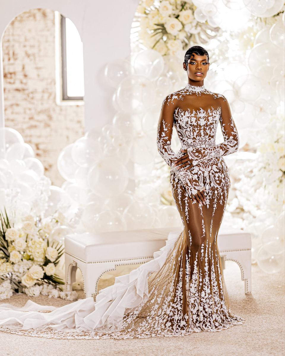 A bride poses in her wedding dress in front of white flowers and balloons.