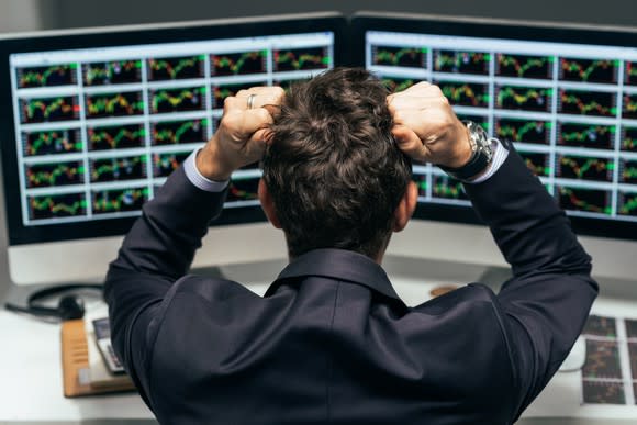 A person looking at two computer screens covered in various charts grabbing their hair in frustration.