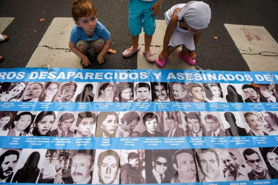 Niños juegan al lado de un cartel con imágenes y nombres de desaparecidos