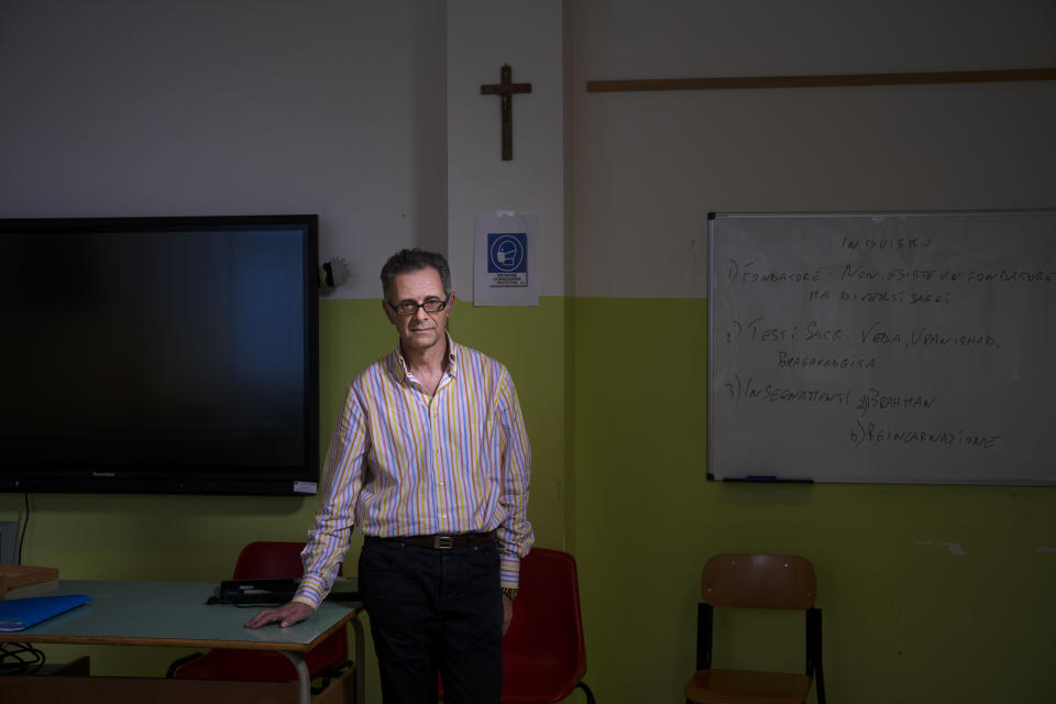 Marco Palareti, who has taught religion for 36 years, poses, Monday, June 5, 2023, in his public school classroom in the provincial capital of Teramo, central Italy, where only 17 of 358 students opted out of his class in the last academic year – mostly migrant children who follow non-Christian religions – and nobody has questioned the crucifix displayed prominently in the classroom. (AP Photo/Domenico Stinellis)