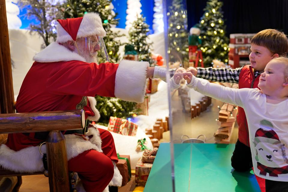 Julianna, 3, and Dylan, 5, Lasczak visit with Santa through a transparent barrier at a Bass Pro Shop in Bridgeport, Conn., Tuesday, Nov. 10, 2020. Santa Claus is coming to the mall — just don't try to sit on his lap. Malls are doing all they can to keep the jolly old man safe from the coronavirus, including banning kids from sitting on his knee, no matter if they've been naughty or nice. (AP Photo/Seth Wenig) ORG XMIT: CTSW607