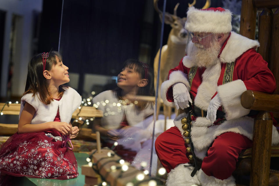Gracelynn Blumenfeld, 8, visits with Santa through a transparent barrier at a Bass Pro Shop in Bridgeport, Conn., on Nov. 10, 2020. In this socially distant holiday season, Santa Claus is still coming to towns (and shopping malls) across America but with a few 2020 rules in effect. (AP Photo/Seth Wenig)