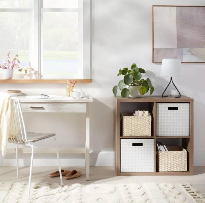 Work desk with lamp, chair, storage cubes with baskets, wall art, plant, and window