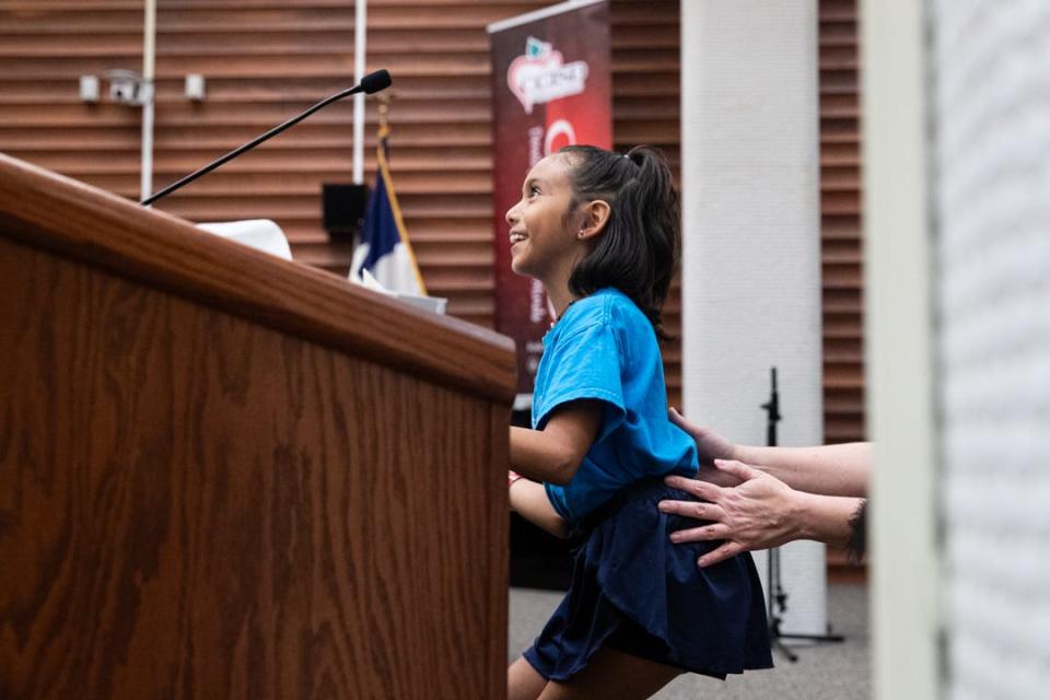 Rachel Beavers, the global problem solving teacher for Windsor Park, helps third grade student Mae West climb onto a stool at a podium to debate community gardens on Tuesday, Oct. 24, 2023, in Corpus Christi, Texas.