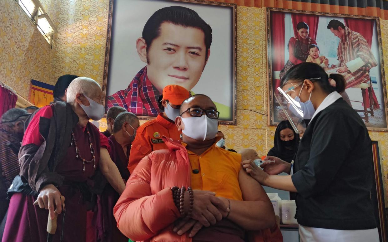 A Buddhist monk receives his vaccine underneath a portrait of King Jigme Khesar Namgyel Wangchuck - Upasana Dahal/AFP