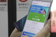 In this April 1, 2020, photo, a passenger holds up a green pass on their phone on a subway train in Wuhan in central China's Hubei province. Green is the "health code" that says a user is symptom-free and it’s required to board a subway, check into a hotel or just enter Wuhan, the central city of 11 million people where the pandemic began in December. (AP Photo/Olivia Zhang)