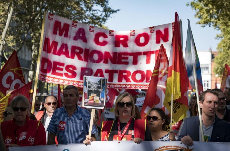 People march with placards, flags and banners in Toulouse. The banner reads: "Macron, puppet of the employers"