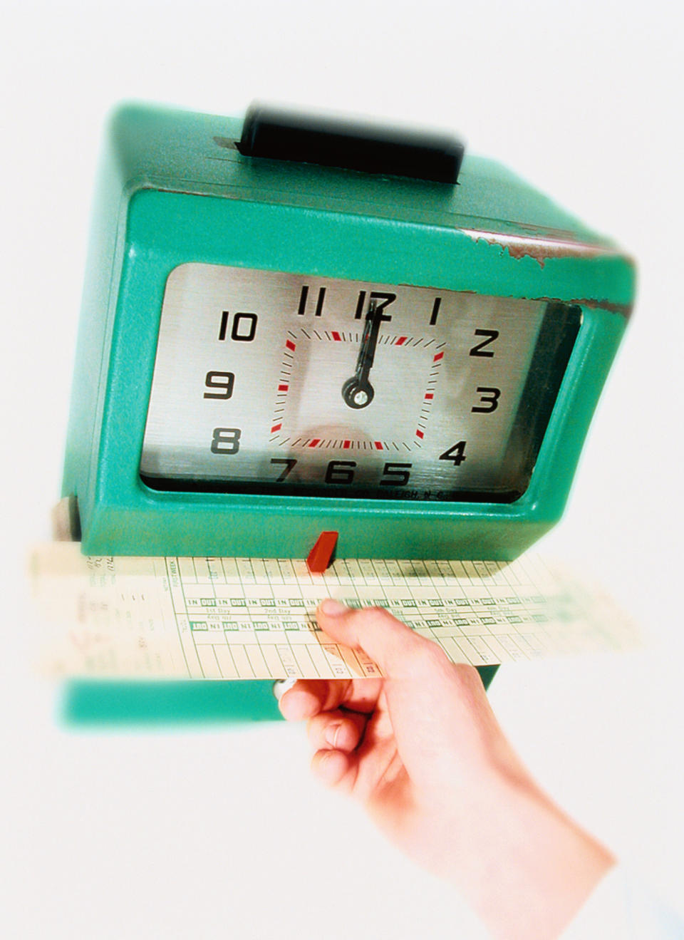 A hand is inserting a time card into a vintage punch clock, marking work hours. The punch clock has visible wear, indicating extensive use