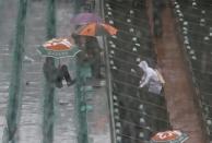 Spectators protect themselves from rain during a men's singles match between Novak Djokovic of Serbia and Joao Sousa of Portugal at the French Open tennis tournament at the Roland Garros stadium in Paris May 26, 2014. REUTERS/Gonzalo Fuentes (FRANCE - Tags: SPORT TENNIS)