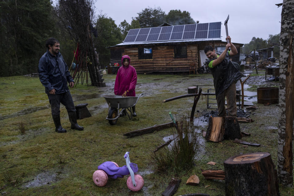 Jaime Uribe Montiel chops firewood as his niece Likarayen Mariantu and a family friend keep him company on ancestral land handed down to Uribe's wife, Millaray Huichalaf, in Carimallin, southern Chile, on Tuesday, June 28, 2022. The Huichalafs have been leading a battle against energy companies and others in a decadelong effort to reclaim their ancestral lands. (AP Photo/Rodrigo Abd)