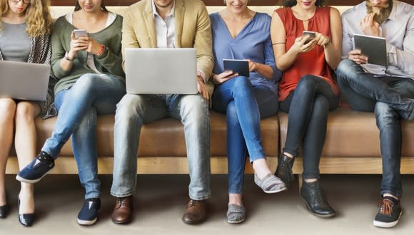 People use laptiops, phones, and tablets sitting in a row.