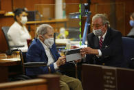 Defense attorney Dick DeGuerin, right, gives Robert Durst a device to read the real time spoken script as he appears in a courtroom as Judge Mark E. Windham gives last instructions to jurors before attorneys begin opening statements at the Los Angeles County Superior Court, Tuesday, May 18, 2021, in Inglewood, Calif. Durst, 78, is charged with one count of murder — in the killing of his best friend, Susan Berman, in 2000 in her Los Angeles home. (Al Seib/Los Angeles Times via AP, Pool)