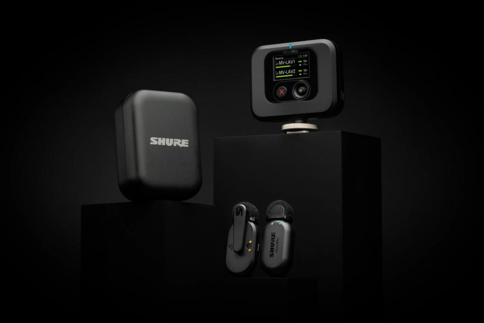 Product image of the Shure MoveMic Two package.  Two wireless neck microphones, charging case and receiver sit on black pedestals against a dramatic black background.