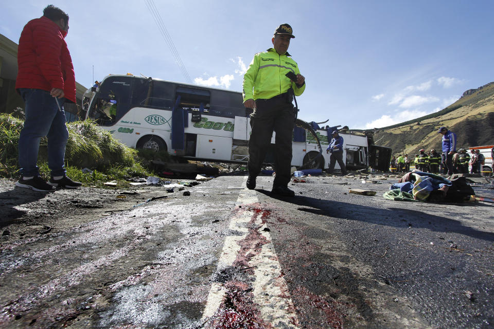 A police officer walks past a Colombian-registered bus traveling to Quito that crashed in Pifo, Ecuador, Tuesday, Aug. 14, 2018. At least 24 people were killed and another 19 injured when a bus careened into another vehicle at high speed and overturned along the Pifo-Papallacta highway, near Ecuador's capital, local officials reported. (AP Photo/Carlos Noriega)