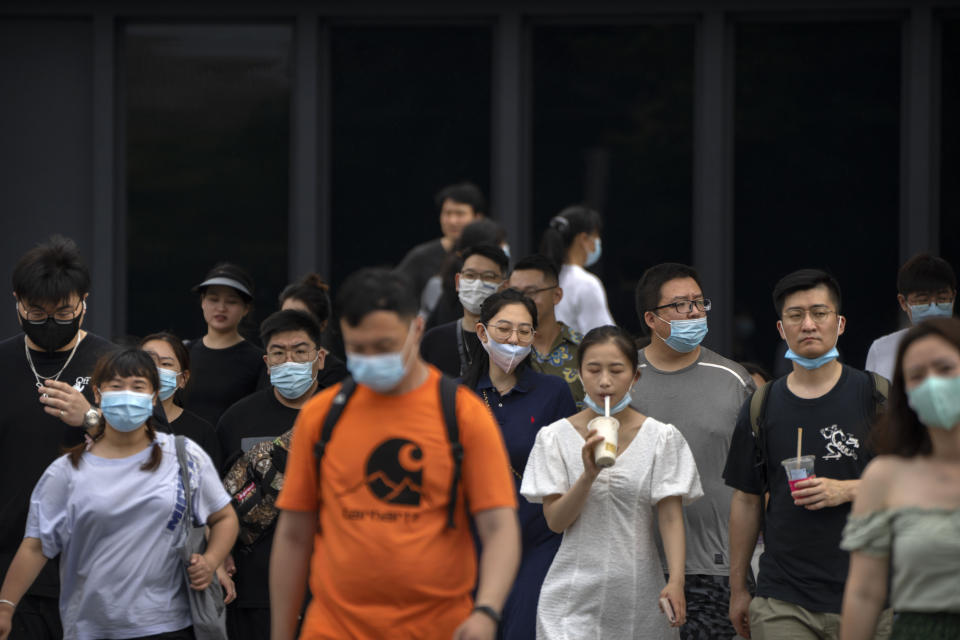 People wearing face masks walk across an intersection in Beijing, Saturday, Aug. 6, 2022. (AP Photo/Mark Schiefelbein)