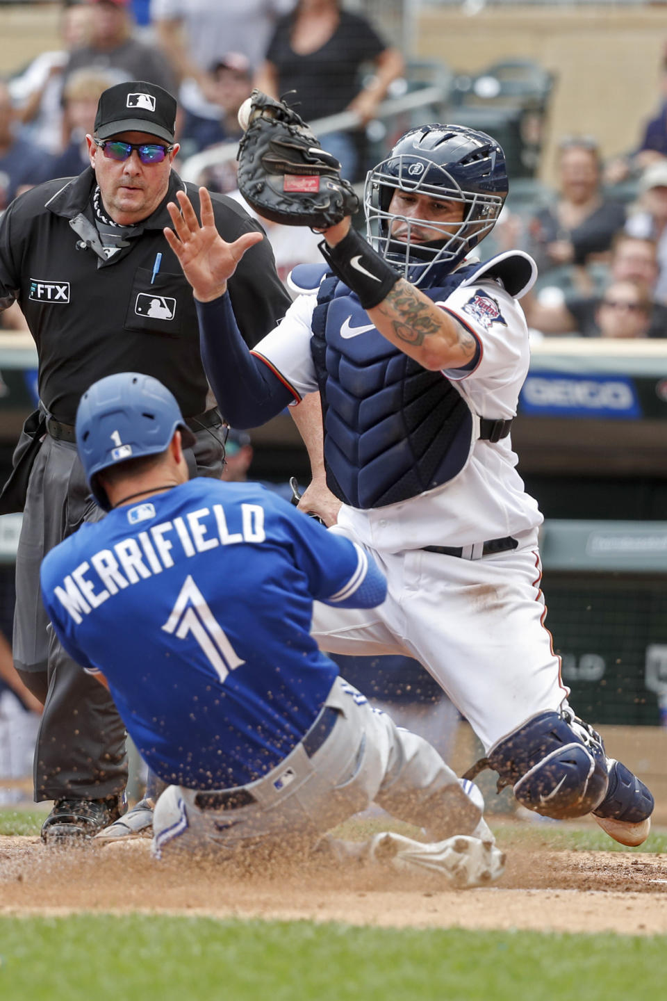 Minnesota Twins catcher Gary Sanchez, right, tags out Toronto Blue Jays' Whit Merrifield (1) who ran from third on a sacrifice fly by Cavan Biggio as home plate umpire Marty Foster, top left, looks on in the 10th inning of a baseball game Sunday, Aug. 7, 2022, in Minneapolis. The play was overturned on review due to Sanchez blocking the plate. (AP Photo/Bruce Kluckhohn)