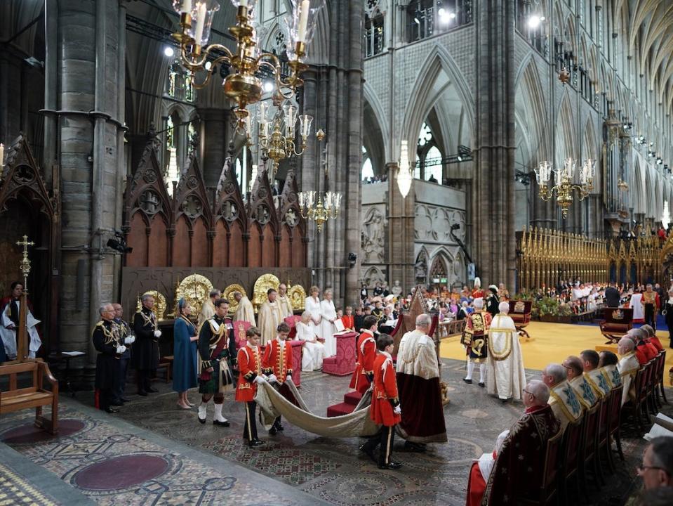 Pages Prince George, Lord Oliver Cholmondley, Nicholas Barclay, and Ralph Tollemache carry the train of King Charles' robe in Westminster Abbey for his coronation.