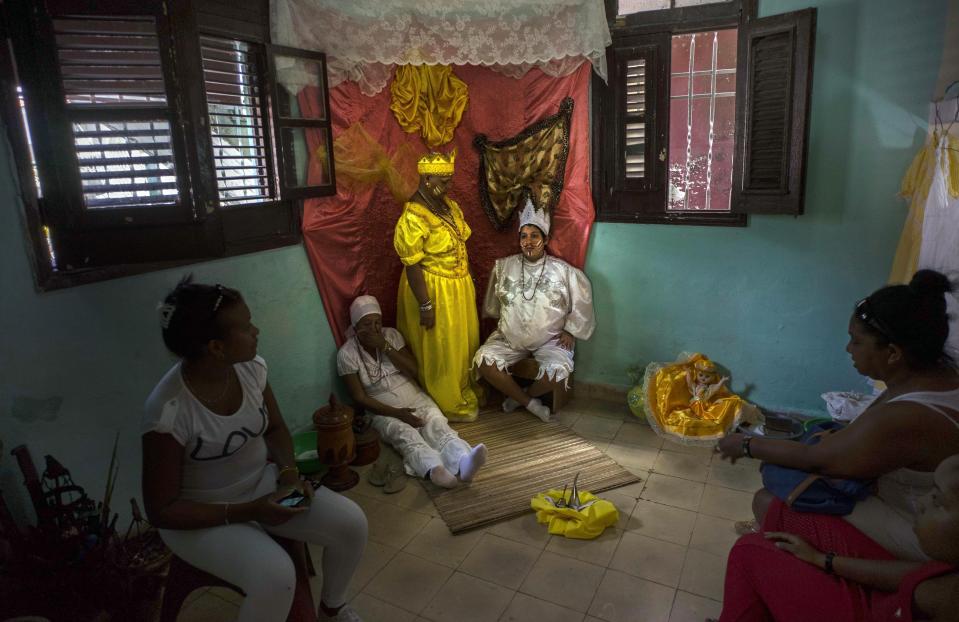 ARCHIVO - Marisa Ramírez Gutiérrez, de pie al centro, se mantiene inmóvil en su trono simbólico portando el vestido de la "Iyawo", o esposa, junto a una mujer embarazada que representa el nacimiento, y su madre, que representa a una mujer que ya dio a luz, dentro de su casa como parte de muchas ceremonias de iniciación para marcar el inicio de su recorrido de un año para convertirse en una sacerdotisa yoruba, el 11 de septiembre de 2015, en La Habana, Cuba. La santería nació como una forma de resistencia silenciosa entre las comunidades de personas negras de Cuba. (AP Foto/Ramón Espinosa, archivo)