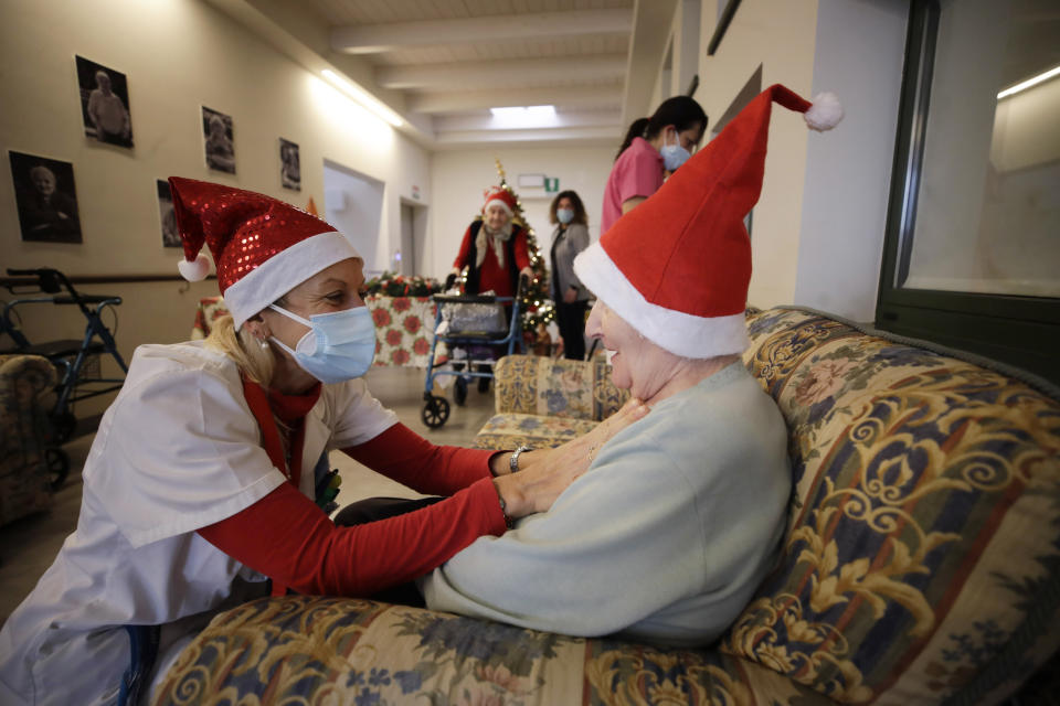 Director Maria Giulia Madaschi, left, talks with Pasqualina Ghilardi, 87, before talking via video call with Caterina Damiano, unrelated to her, who bought and sent her a Christmas present through an organization dubbed "Santa's Grandchildren", at the Martino Zanchi nursing home in Alzano Lombardo, one of the area that most suffered the first wave of COVID-19, in northern Italy, Saturday, Dec. 19, 2020. (AP Photo/Luca Bruno)