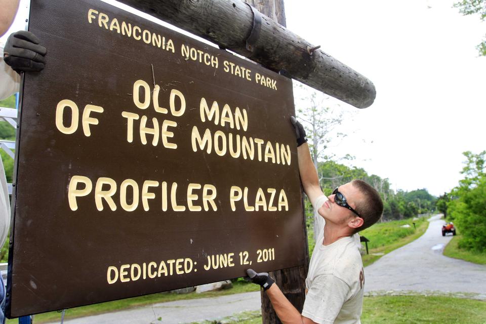 FILE - Cameron Pearson helps hang a sign at the base of Cannon Mountain Thursday, June 9, 2011, in Franconia, N.H. Two decades after New Hampshire’s famed Old Man of the Mountain crumbled to pieces, the state is paying tribute to the granite profile that symbolizes its independence and still adorns its license plates with new geological research, poetry, a song, and a scavenger hunt. (AP Photo/Jim Cole, File)