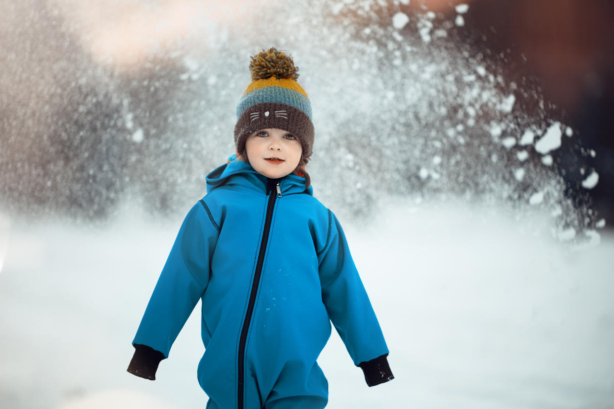 Child in coat and knit hat standing in snow.