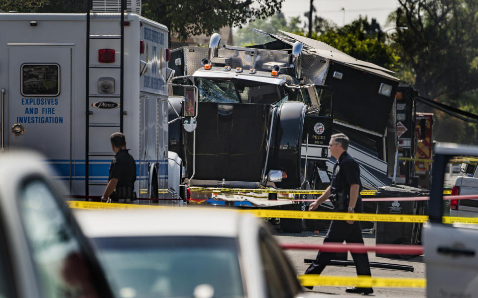 FILE - In this July 1, 2021 file photo police officers walk past the remains of an armored Los Angeles Police Department tractor-trailer, after illegal fireworks seized at a home exploded, in South Los Angeles. Arturo Ceja III, the man who stockpiled illegal fireworks in his South Los Angeles backyard — which were later improperly detonated by police, likely causing the massive blast in late June that rocked a neighborhood and injured 17 people — now faces a decade in federal prison. Ceja pleaded guilty Monday, Aug. 30 to one count of transportation of explosives without a license. (AP Photo/Damian Dovarganes, File)