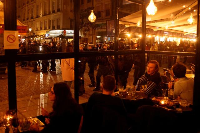 People sit in a bar as riot police stand guard during a demonstration against the French government's pension reform, in Paris (REUTERS)