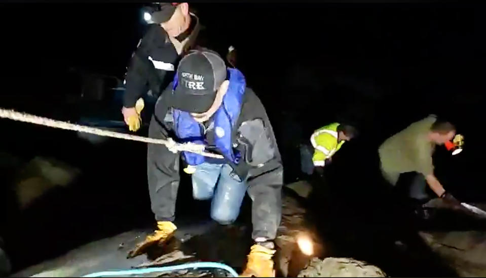 This photo from video provided by Rob Gensorek of Basin Tackle Charleston shows firefighters rescuing the crew from a capsized crab boat in the harbor at Coos Bay, Ore., late Tuesday evening, Jan. 14, 2020. Three men were in good condition early Wednesday after being cut from inside the hull of the capsized boat. The 38-foot (11-meter) Pacific Miner was flipped upside-down by large waves late Tuesday and then got caught on rocks in a jetty in Coos Bay as the tide went out. A U.S. Coast Guard helicopter on a routine training mission spotted the vessel and launched a rescue, the agency said in a news release. (Rob Gensorek of Basin Tackle Charleston via AP)