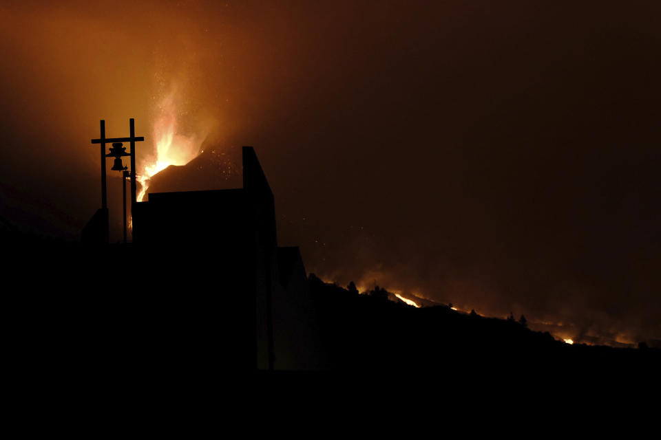 A volcano continues to spew out lava behind a church in Tajulla on the Canary island of La Palma, Spain in the early hours of Sunday, Oct. 10, 2021. A new river of lava has belched out from the La Palma volcano, spreading more destruction on the Atlantic Ocean island where molten rock streams have already engulfed over 1,000 buildings. The partial collapse of the volcanic cone has sent a new lava stream heading toward the western shore of the island. (AP Photo/Daniel Roca)